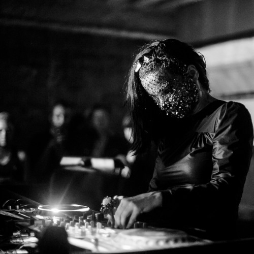 a woman wearing a beaded mask onstage djing