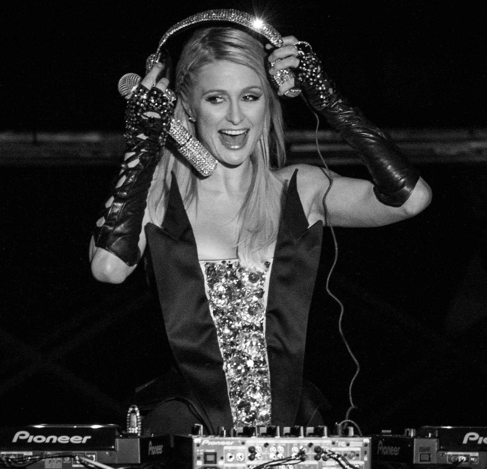 a woman on stage smiling with her hands on DJing headphones she is wearing