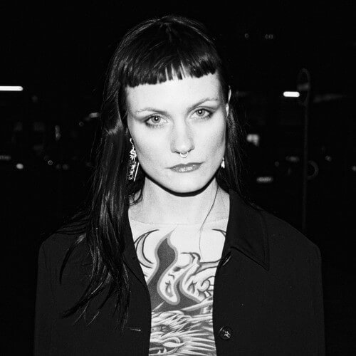 a woman with a straight black fringe and shaved sideburns looking forwards